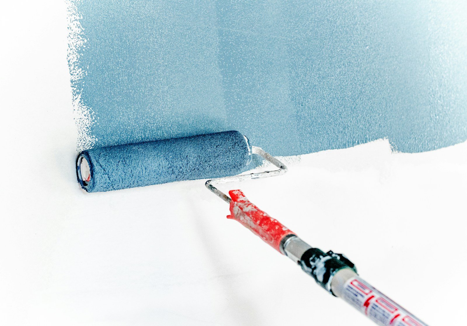 Paint roller applying blue paint evenly to an interior wall