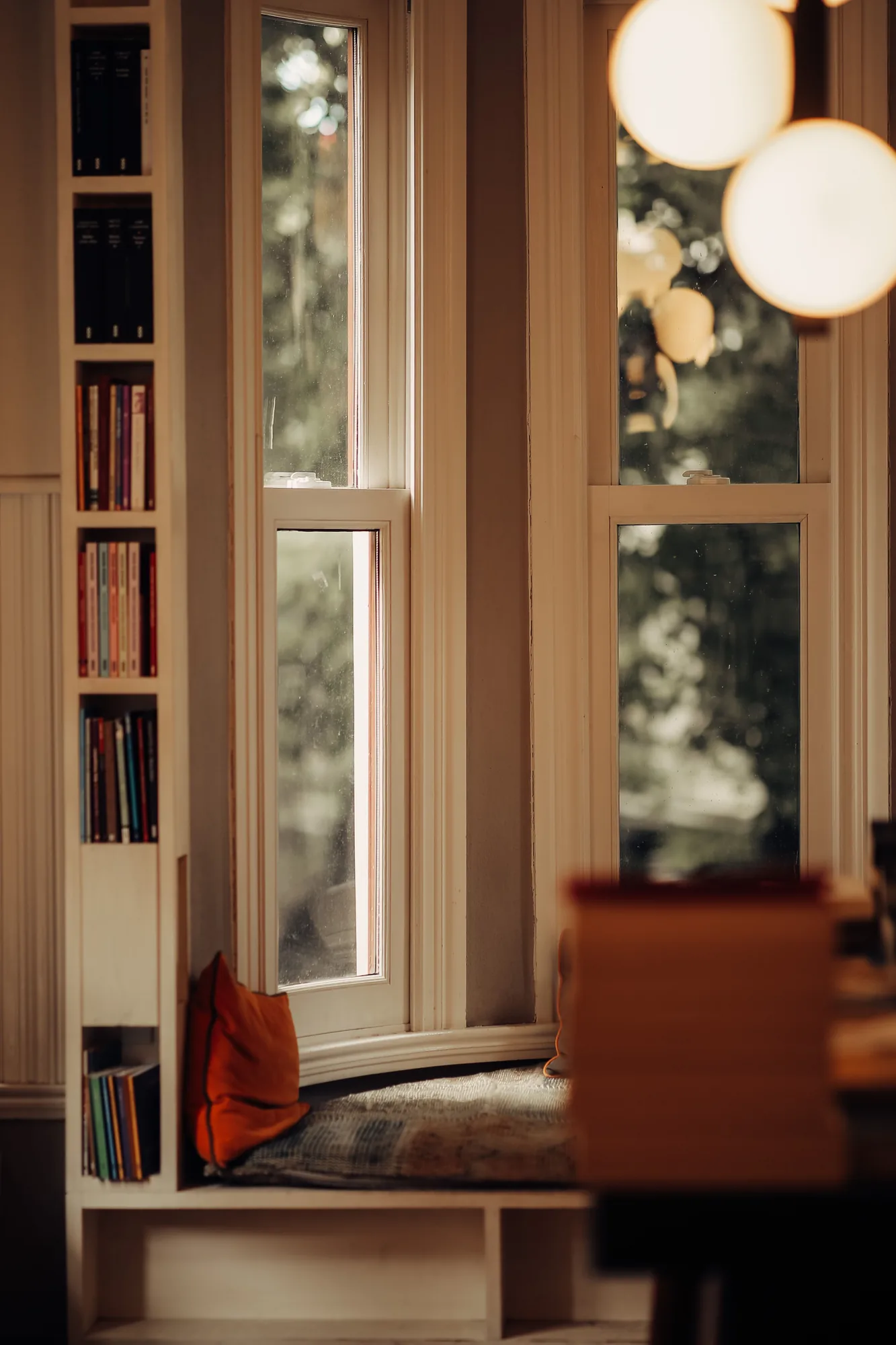 Warm reading corner beside a window with narrow book storage